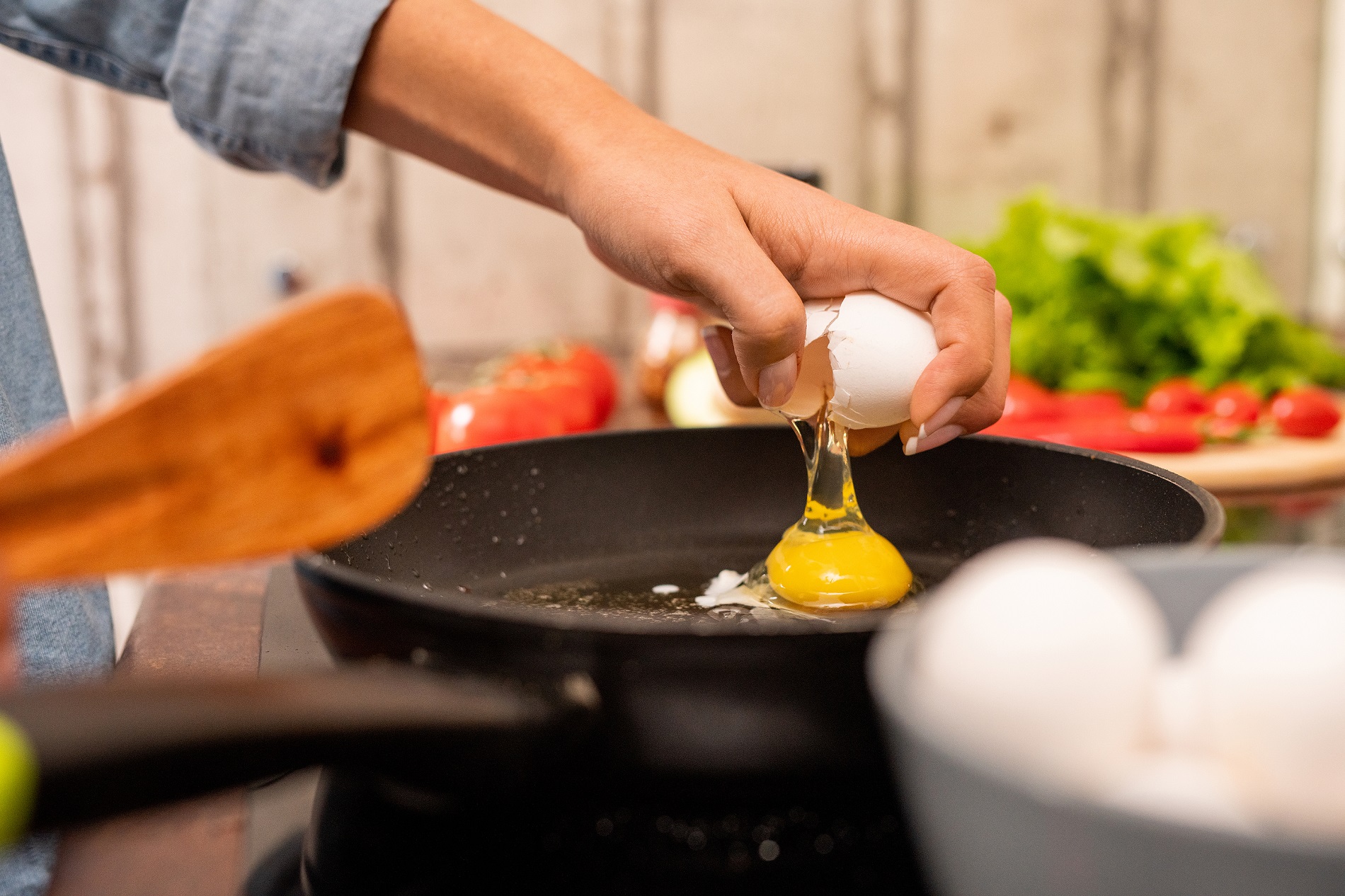 Hand of young woman breaking fresh egg on frying pan standing on electric stove while cooking breakfast in the morning